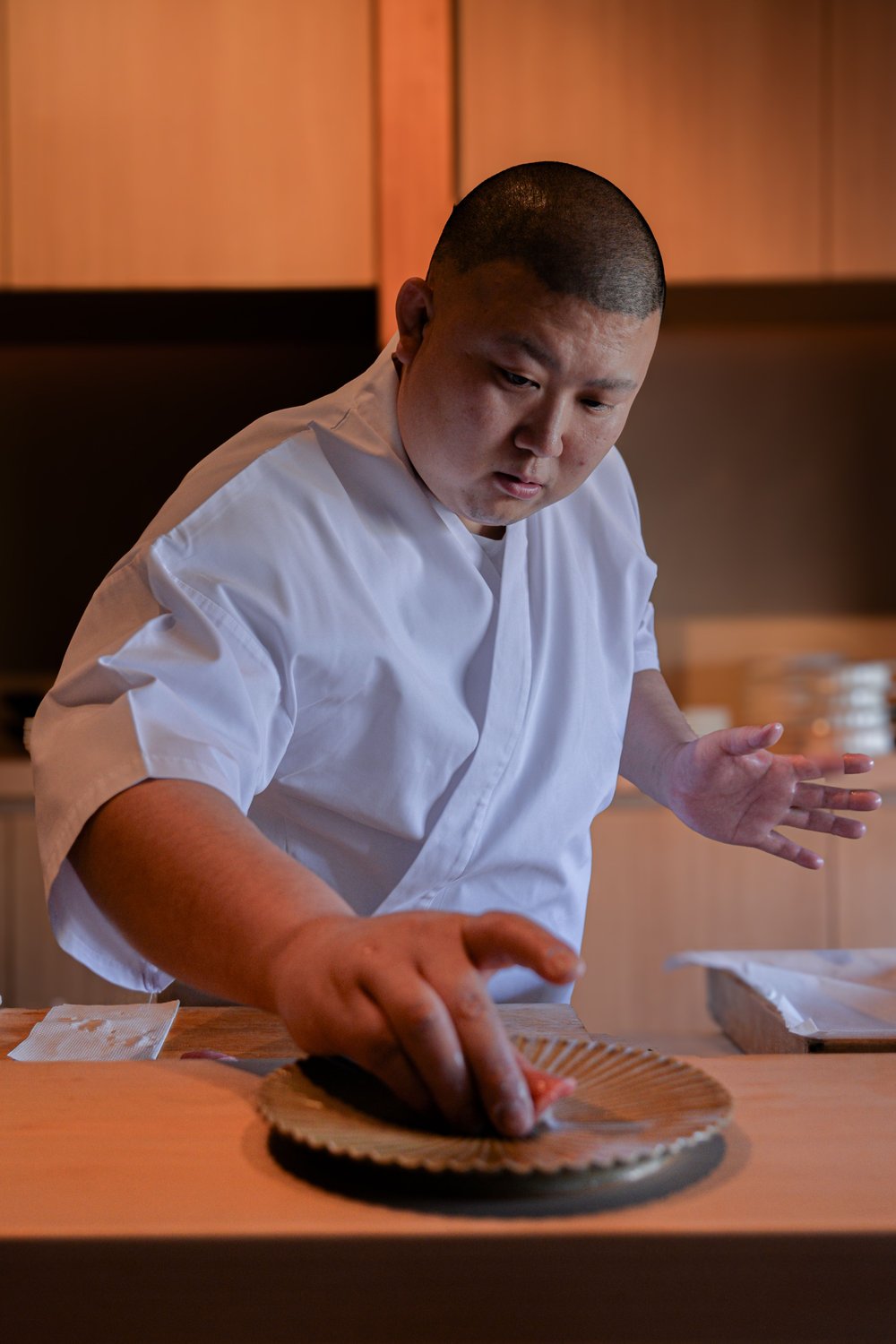 調理場で、皿の上の料理に手を伸ばす料理人